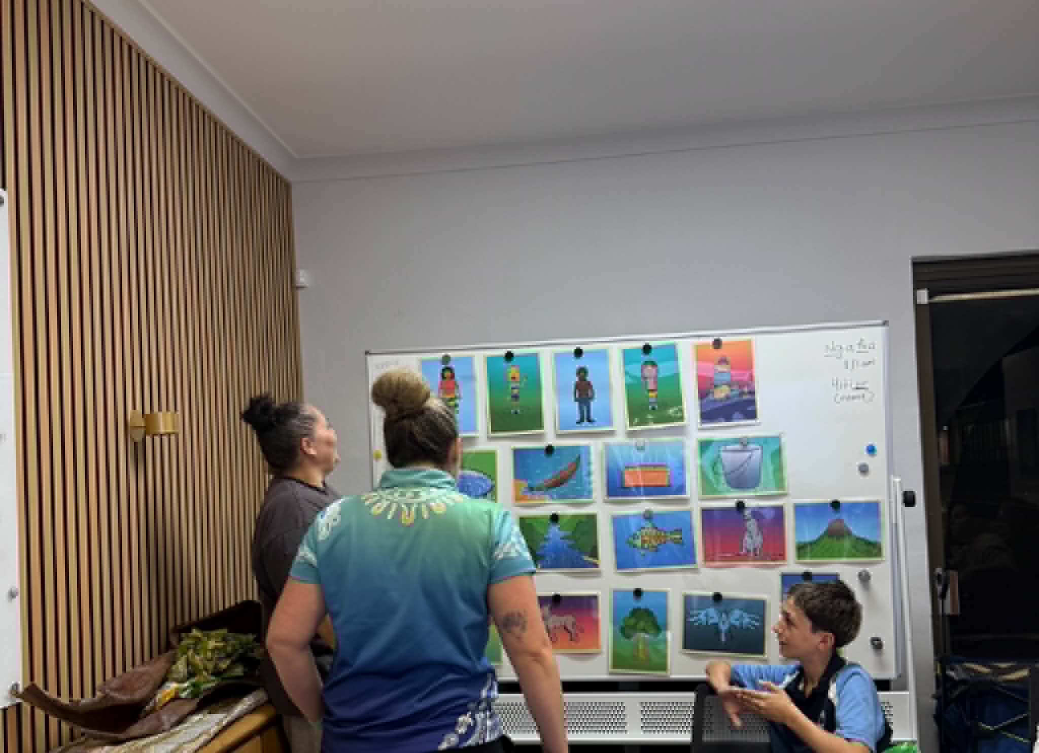 A Gathang teacher pointing to a board of images and language words while a community member looks on during a language class
