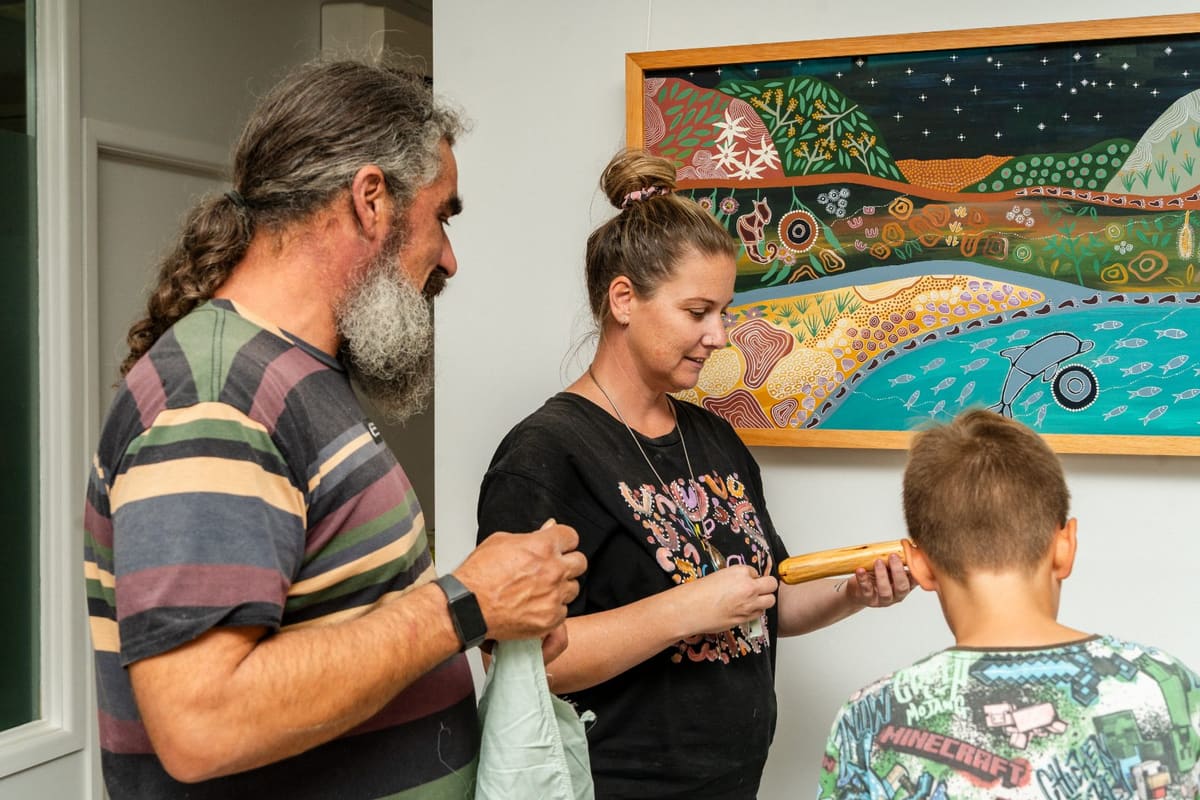 Family sharing a carved clapstick beside community artwork